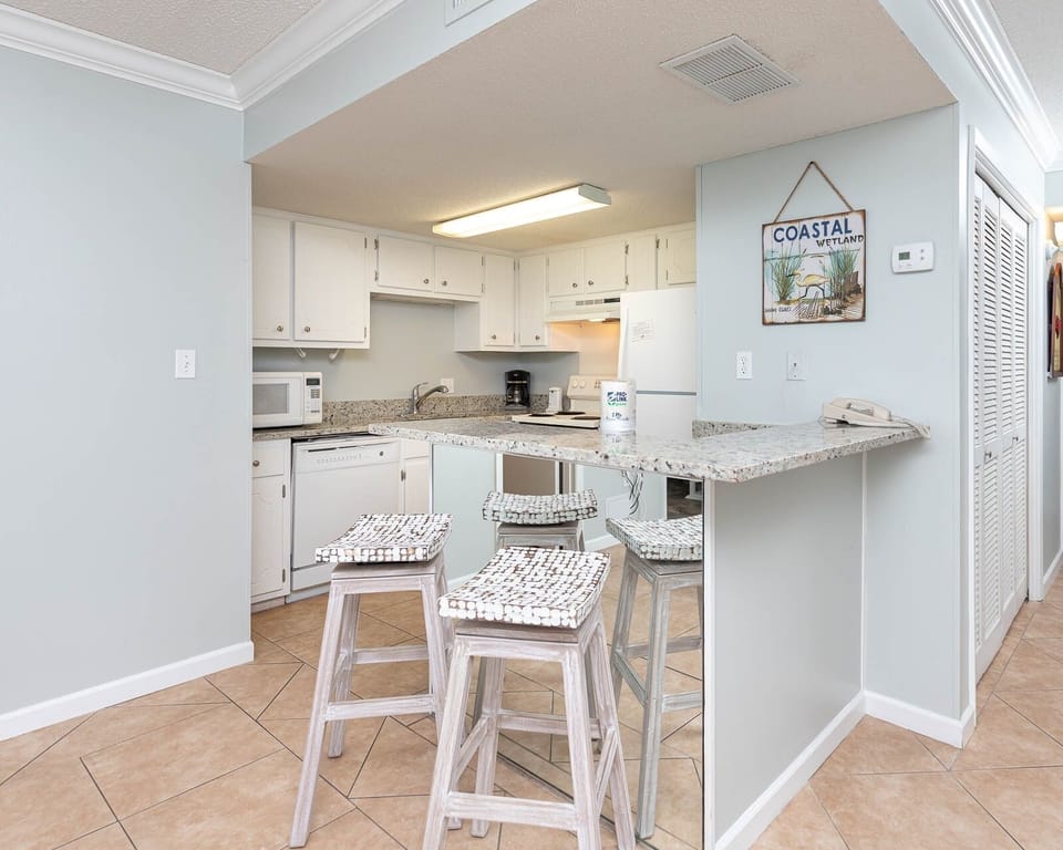 The kitchen features light cabinetry, a breakfast bar, and a cozy coastal decor, perfect for meal prep and gatherings