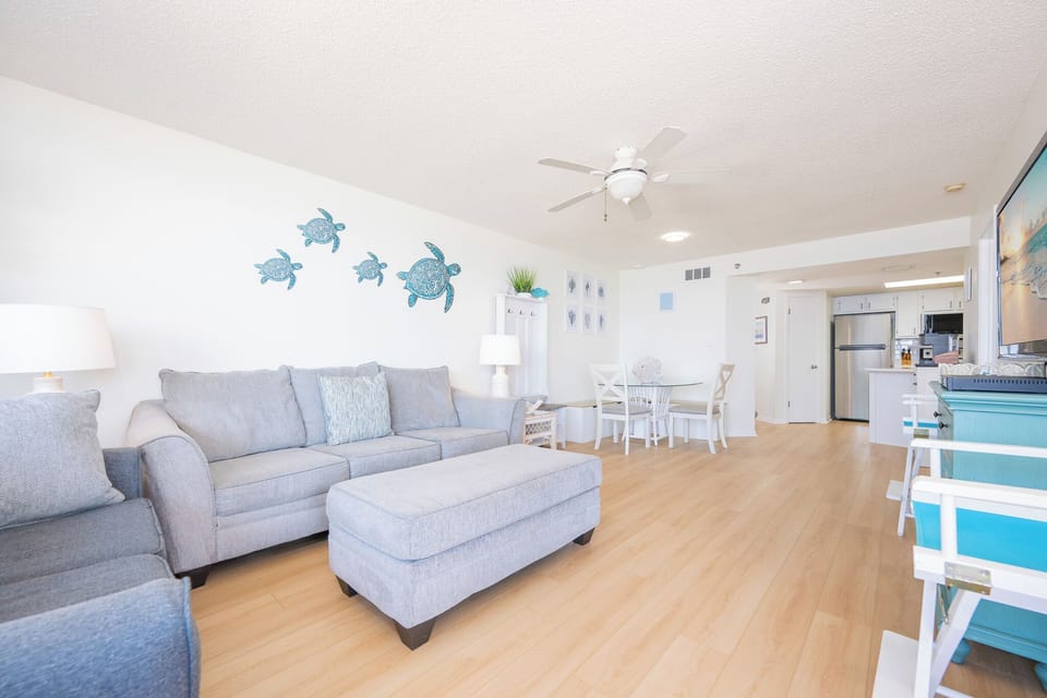 Spacious living area features a comfortable gray sofa, stylish dining set, and a view of the beach through large glass doors
