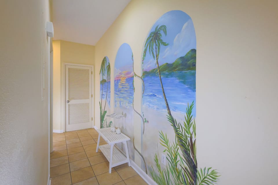 A vibrant mural of palm trees and a serene beach scene enhances the welcoming hallway, complemented by a white side table