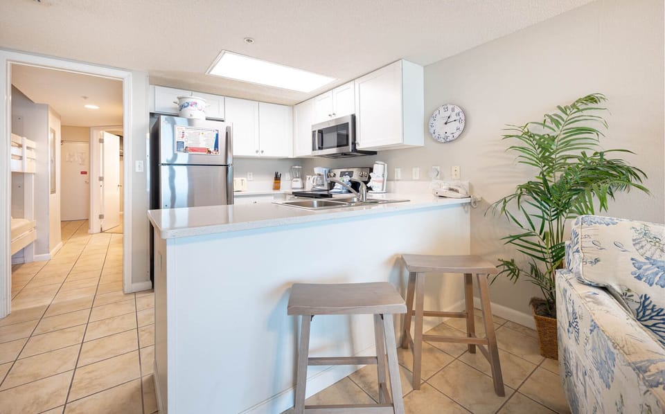 Gather at the kitchen bar with two stools, surrounded by bright cabinetry and a view into the welcoming living space