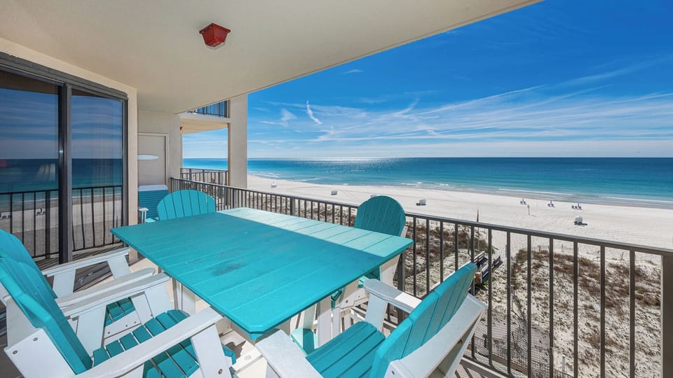 Vibrant turquoise chairs surround a table on your balcony as gentle waves shimmer along the wide beach below