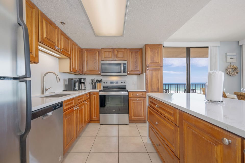 You prepare fresh meals in the kitchen surrounded by rich wood cabinets and a sparkling countertop view of the coast