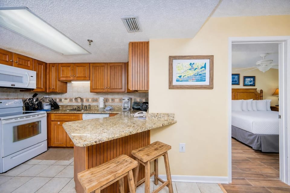 The kitchen features warm wood cabinetry, granite countertops, and a breakfast bar with two wooden stools