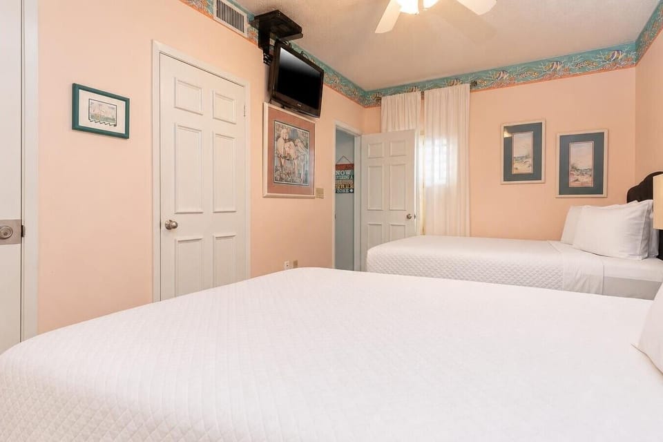 Enjoy restful nights in this guest bedroom with two cozy queen beds, coastal artwork, and soft natural light