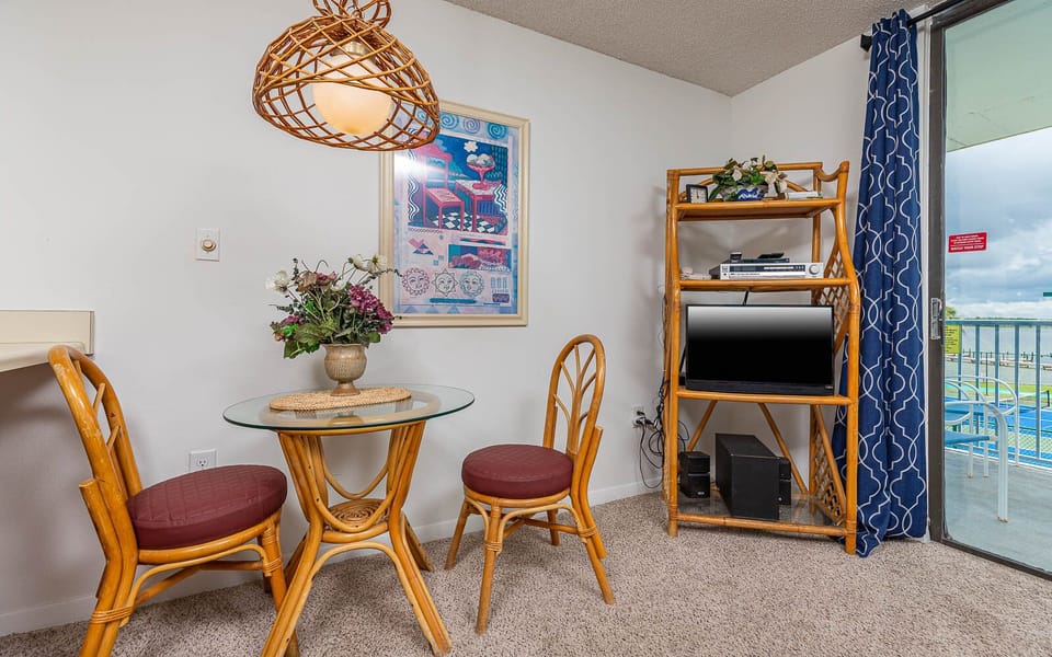 This cozy dining area features a glass table, wicker chairs, and a TV, with a lovely view of the lagoon outside