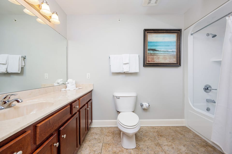 This bathroom features elegant cabinetry, a spacious countertop, and a serene beach-themed artwork for a refreshing retreat