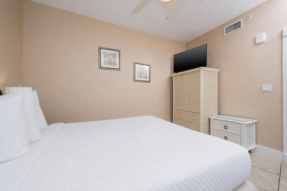 This cozy bedroom features a plush white bed, a TV for entertainment, and tasteful decor for a relaxing stay