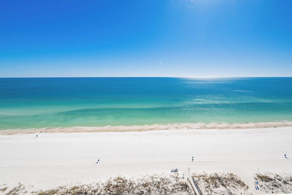Bright blue sky stretches above the shore where gentle waves lap and laughter drifts on the breeze