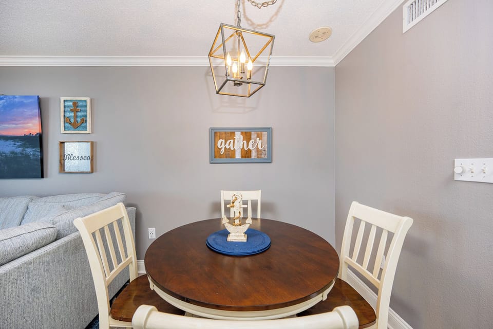 Cozy dining area features a round wooden table with a blue placemat, surrounded by white chairs and nautical decor