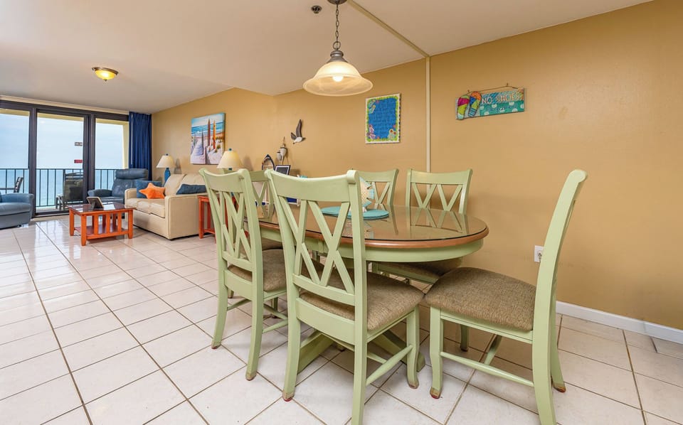 Dining area with a round table, colorful decor, and a view of the beach off the balcony through large windows