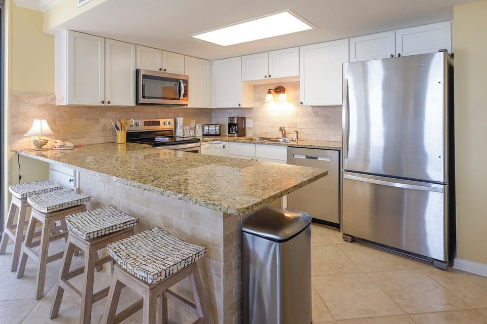 Modern kitchen features a spacious granite countertop with seating, stainless appliances, and warm lighting