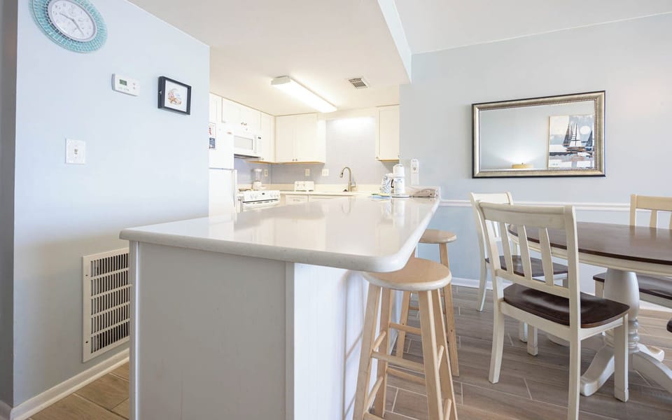 This kitchen features sleek white cabinetry, a spacious countertop, and a dining area, perfect for enjoying meals together