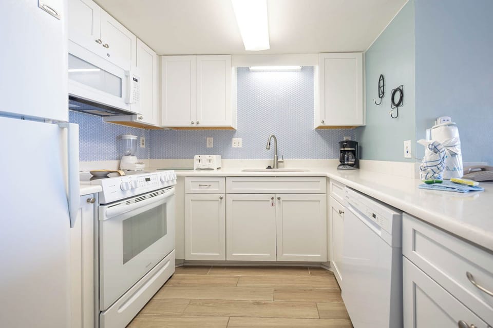 This kitchen features sleek white cabinets, modern appliances, and a stylish blue backsplash, perfect for culinary adventures