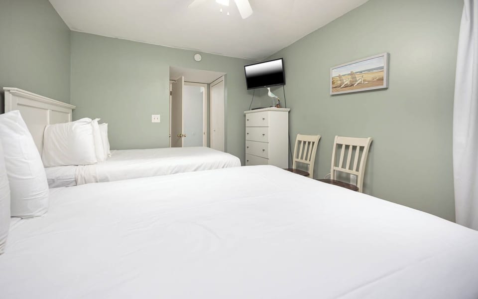 This guest bedroom features two comfortable beds, a mounted TV, and soft green walls, creating a relaxing atmosphere