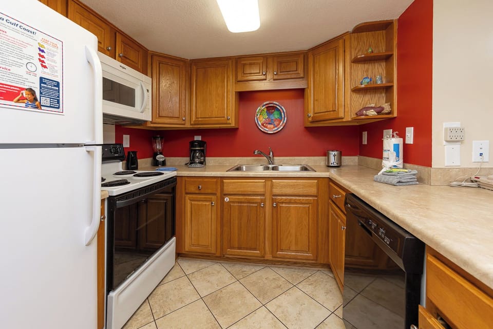 Cozy kitchen featuring warm wooden cabinets, essential appliances, and a vibrant red accent wall for a welcoming atmosphere