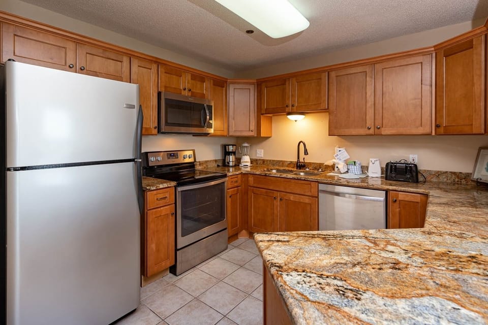 Prepare meals in this inviting kitchen featuring wooden cabinetry, granite countertops, and stainless appliances