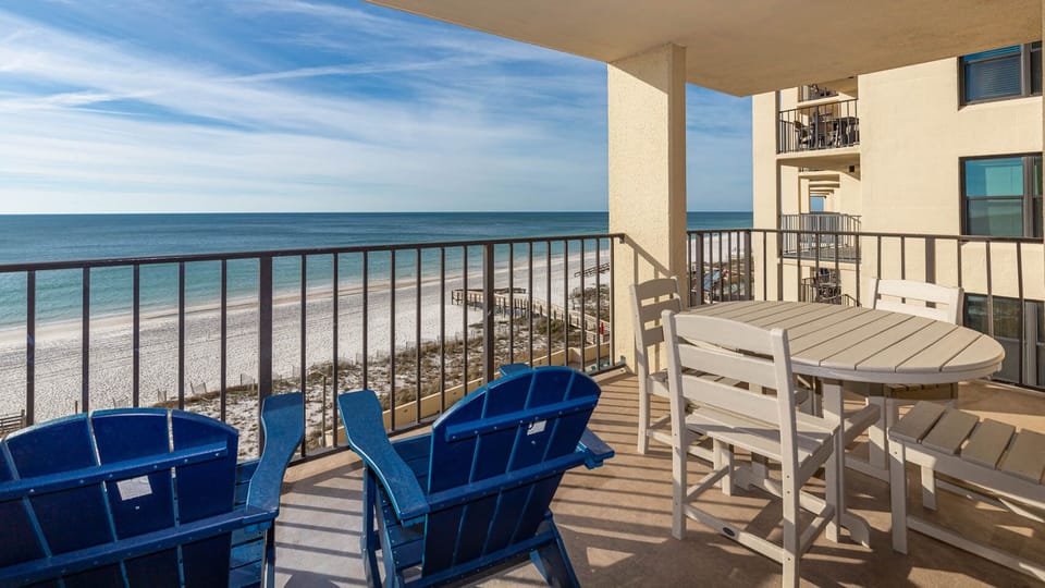 Balcony featuring blue Adirondack chairs and a round table, offering a picturesque view of the beach and tranquil waters