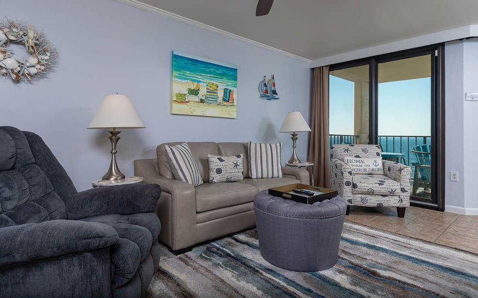 The living room features a light-colored sofa with full-size sleeper, a cozy armchair, and a view of the beachfront