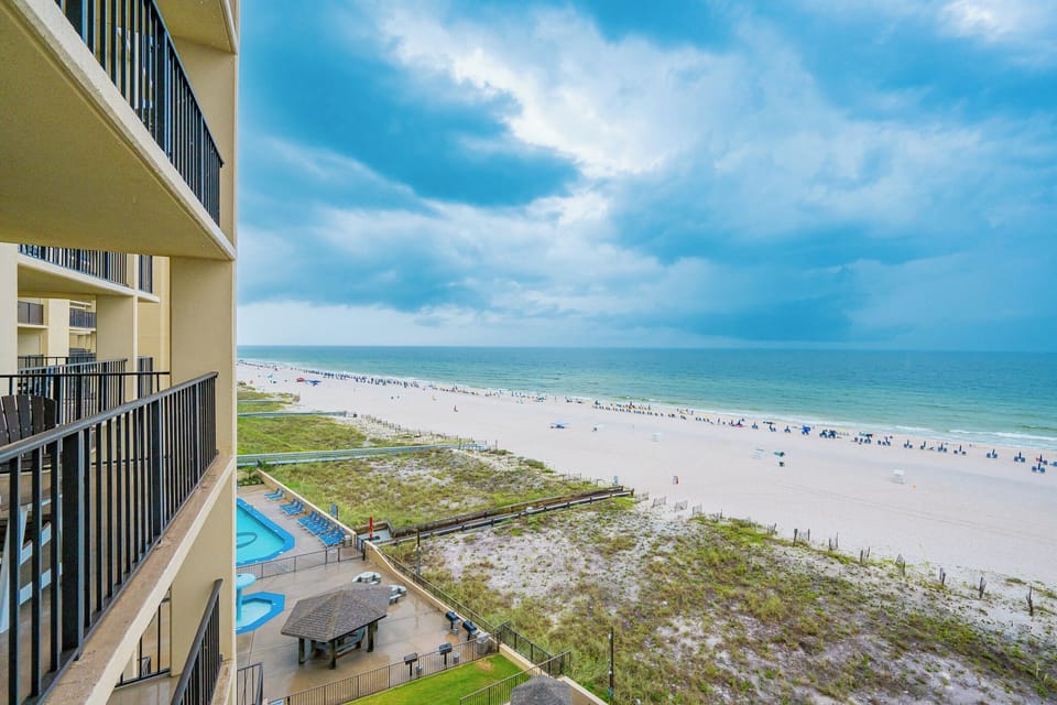 The balcony view showcases the beach front with lounge chairs lining the shore and a glimpse of the pool area below