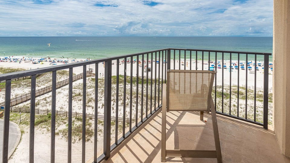 Relax on the balcony with a view of the beach and vibrant umbrellas dotting the shore, perfect for unwinding in the sun