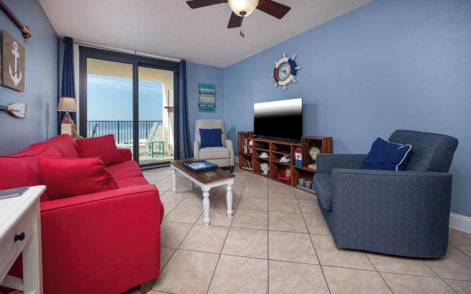 Living room with red sofas and queen sleeper, a large TV, and a balcony offering a beautiful coastal view