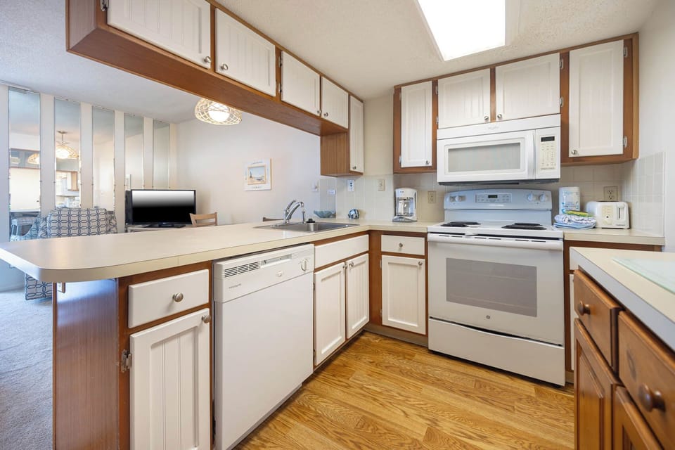 The kitchen features white cabinetry, essential appliances, and a view into the living area with a TV, perfect for gatherings