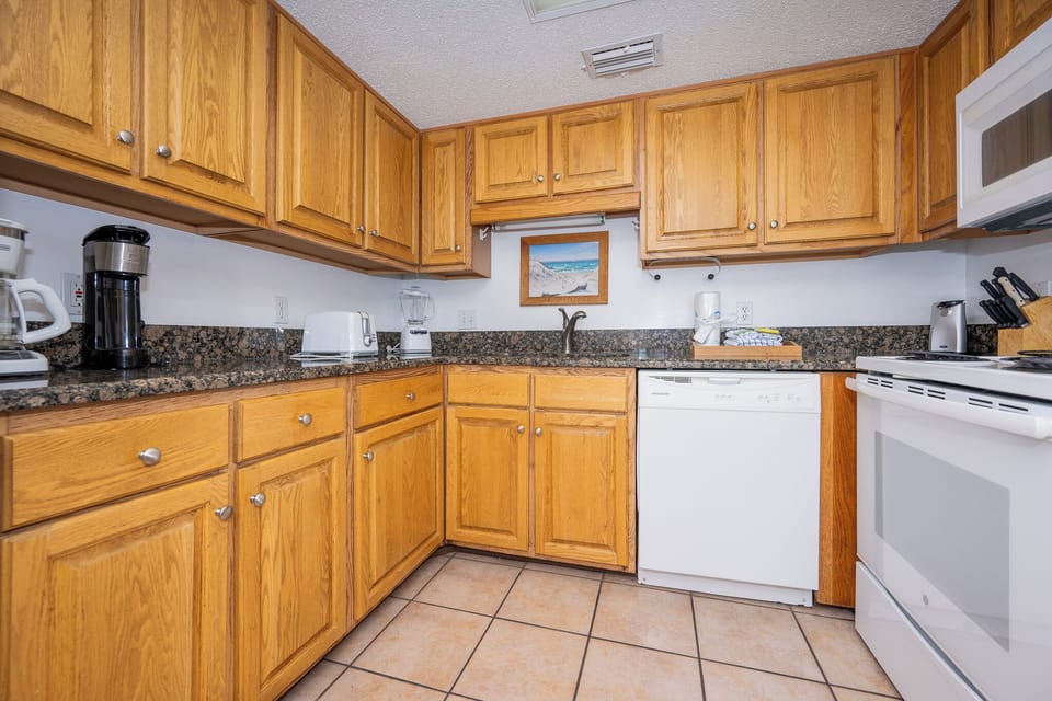 The kitchen features warm wood cabinetry, granite countertops, coffee station, and essential appliances