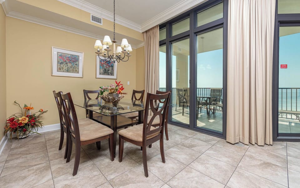 Bright dining area with a glass table, elegant decor, and expansive views of the coastline through large windows