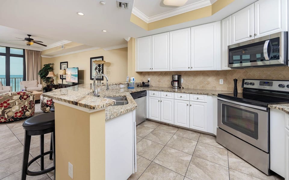 Modern kitchen with granite countertops, stainless appliances, and a view of the living area and beach beyond
