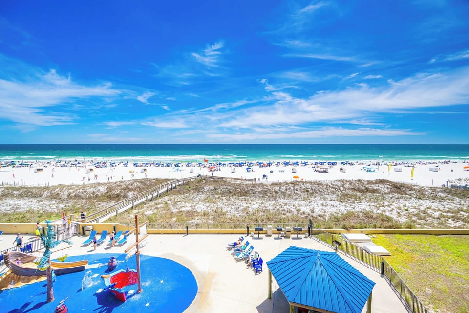 Kids laugh and splash nearby as you relax poolside under deep blue skies by the beach coast