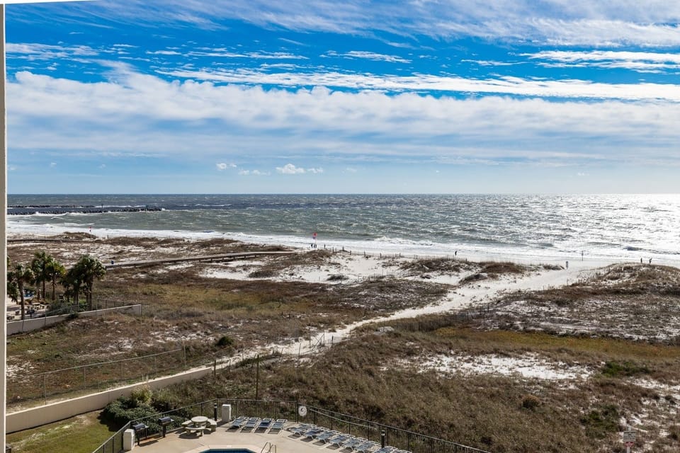 Expansive view of the beach with waves lapping against the shore and the jetties in the distance, framed by lush greenery