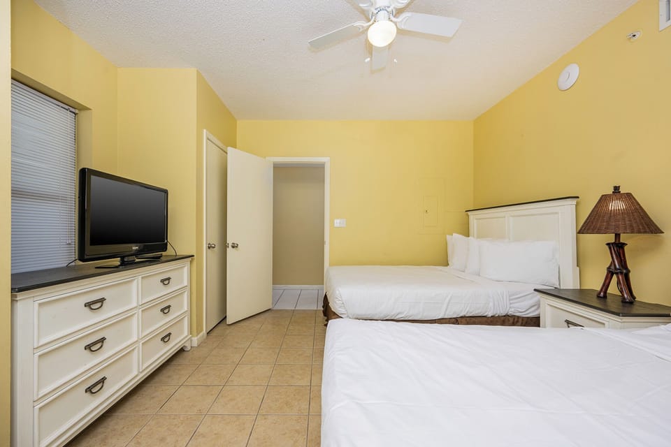 Relax in this cheerful guest room featuring double beds, a TV, and warm yellow walls for a welcoming atmosphere