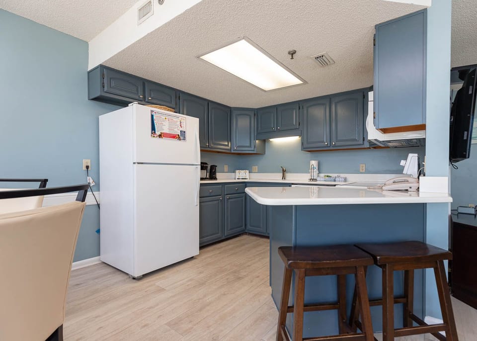 Kitchen featuring blue cabinetry, a white refrigerator, and a spacious countertop with two wooden stools for casual dining