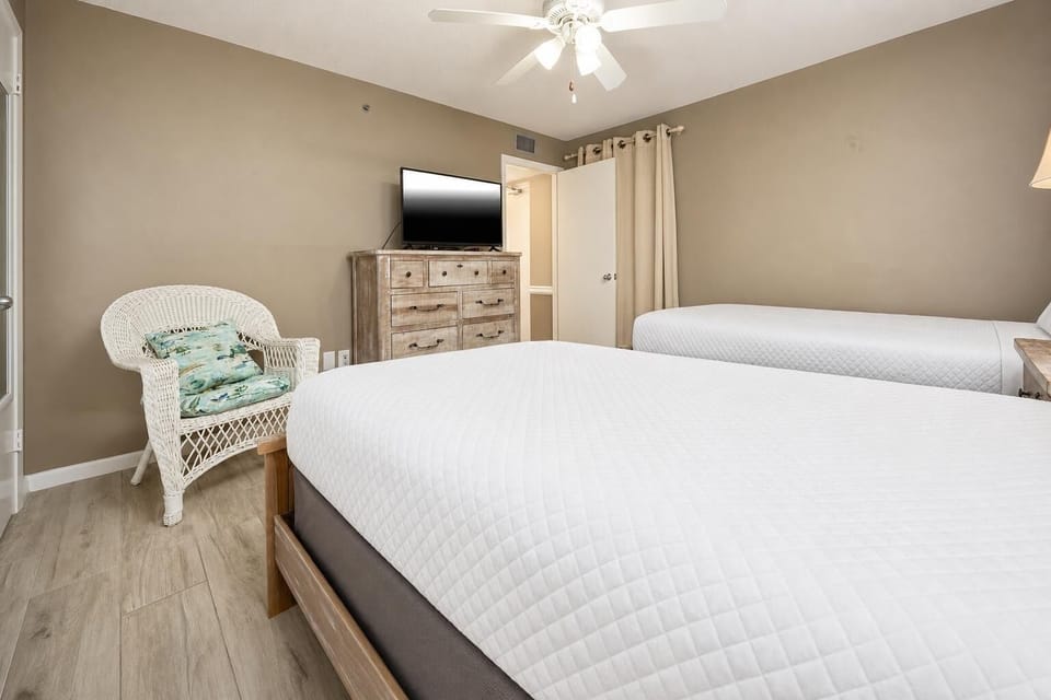 This cozy guest bedroom features two beds, a stylish dresser, and a relaxing wicker chair, perfect for unwinding