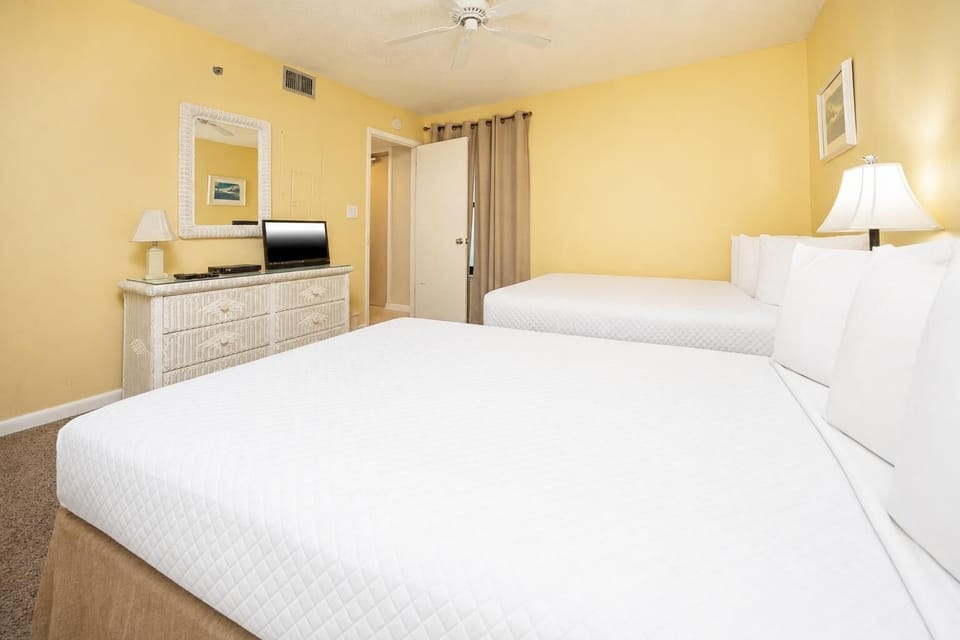 Bright and inviting guest bedroom featuring two comfortable full beds, a TV, and cheerful yellow walls for a cozy retreat