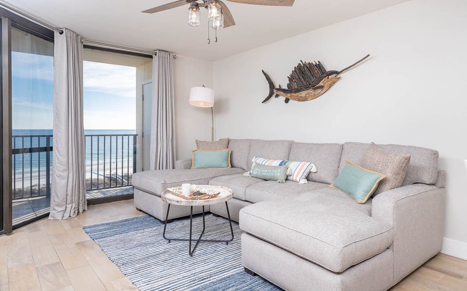 Living area features a large sectional sofa with colorful pillows, a stylish coffee table, and expansive gulf views