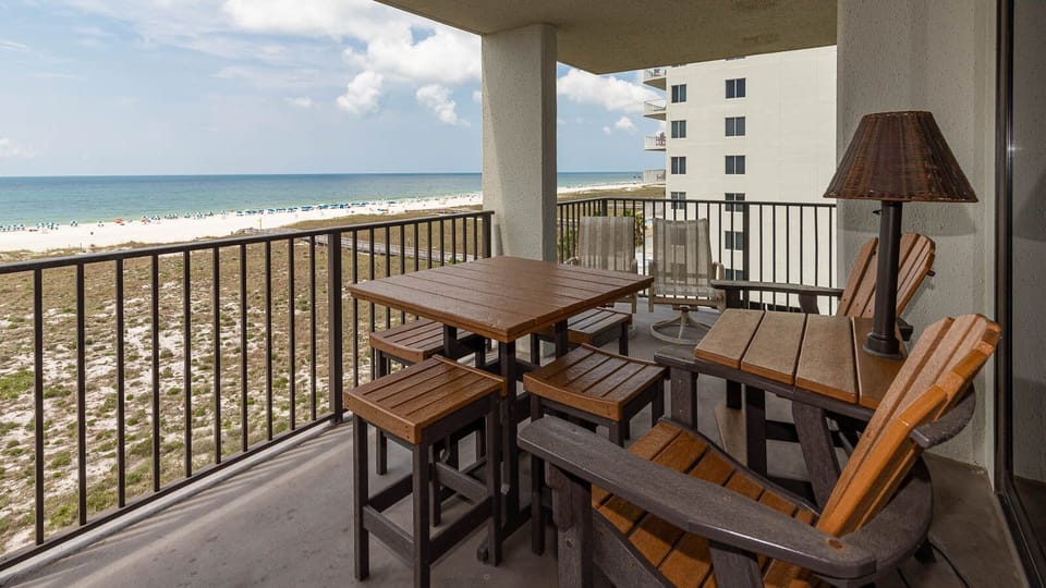 Balcony seating area features a wooden table and chairs, overlooking the beach with vibrant umbrellas dotting the shoreline