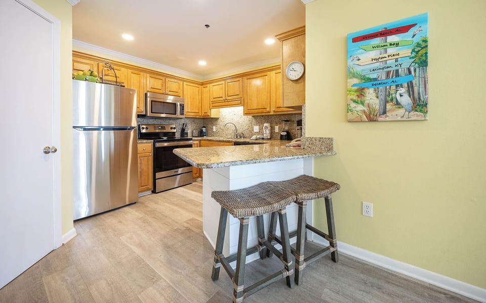 The kitchen features warm wooden cabinetry, granite countertops, stainless appliances, and a breakfast bar with seating
