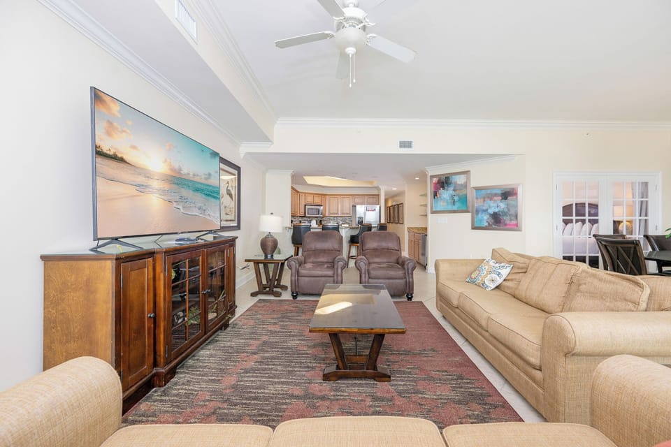 Bright and inviting living room featuring a large TV, queen sofa-sleeper, cozy seating, and a view into the kitchen area
