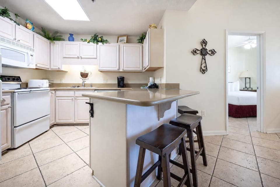 Bright kitchen area features light cabinetry, a breakfast bar with seating, and white appliances