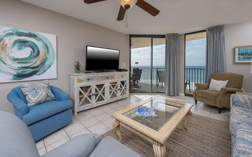 The inviting living area features a blue armchair, a stylish coffee table, and a large window showcasing the beach front