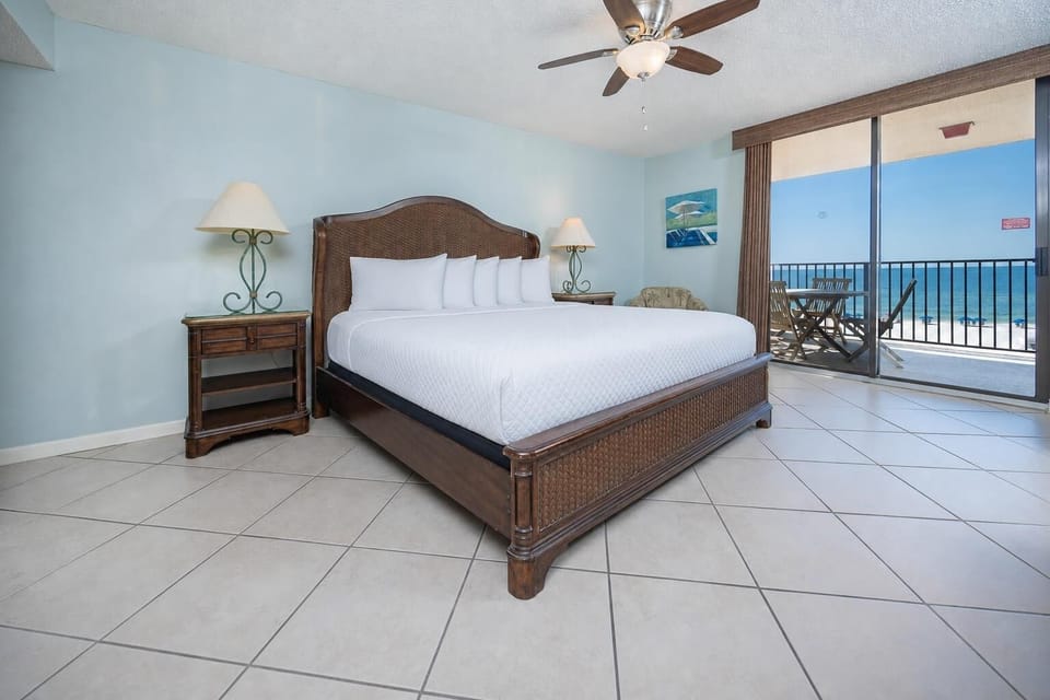 Bright master bedroom featuring a king bed, tropical decor, and a private balcony with a serene beachfront view