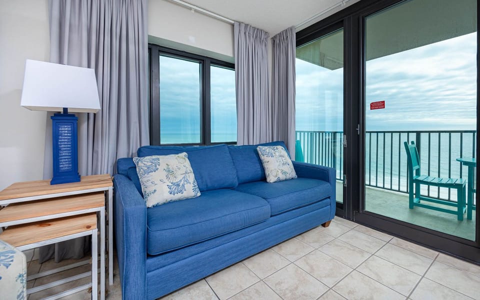 Relax on the blue sofa with queen sleeper while enjoying beach views from the balcony