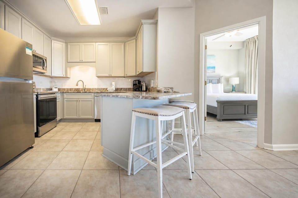 Modern kitchen features light cabinetry, a breakfast bar with seating, and a view into the inviting master bedroom beyond