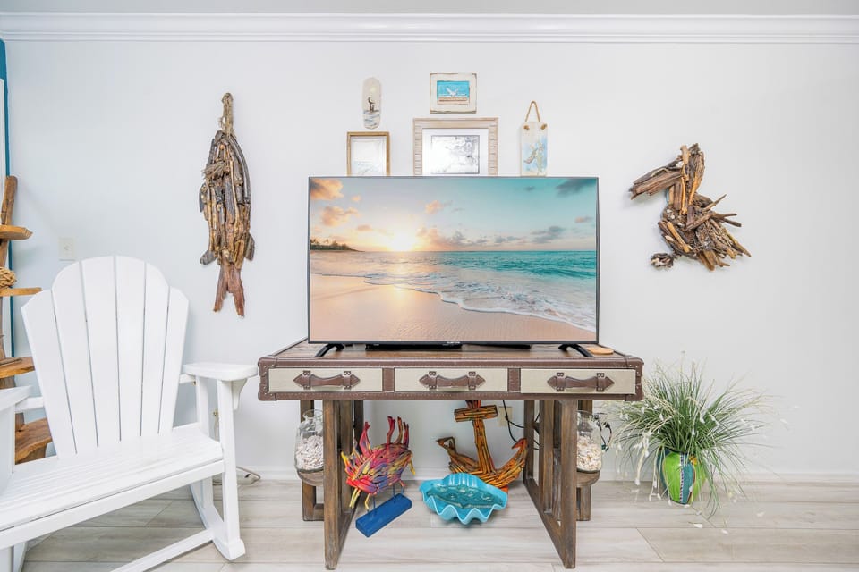 This inviting living area features a large TV, coastal decor, and a comfortable white chair, perfect for relaxation