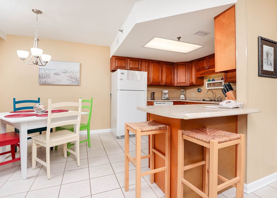 Kitchen with warm wooden cabinetry, a breakfast bar, and a colorful dining area with a white table and vibrant chairs