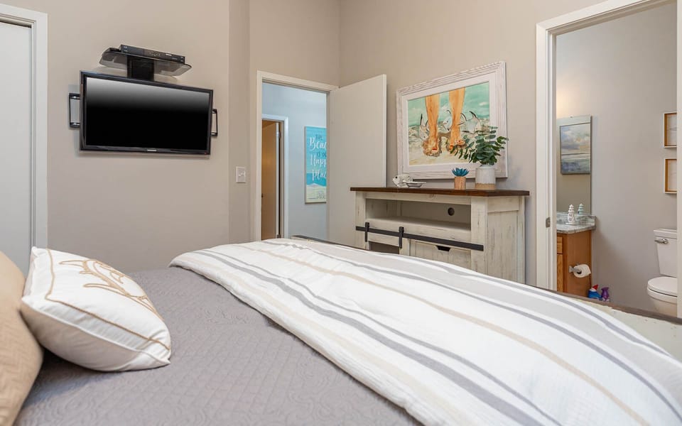 Inviting guest bedroom featuring a queen bed, wall TV, decorative art, and a stylish dresser with the guest bath in view