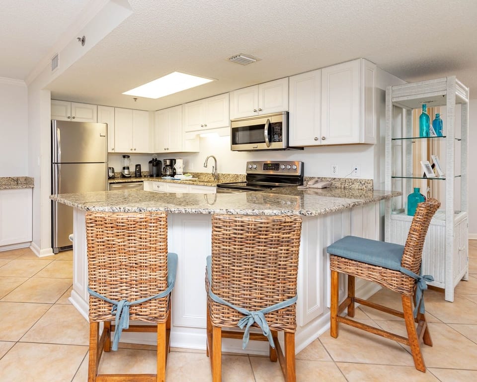 Bright kitchen features granite countertops, modern appliances, coffee corner, and a breakfast bar with woven chairs