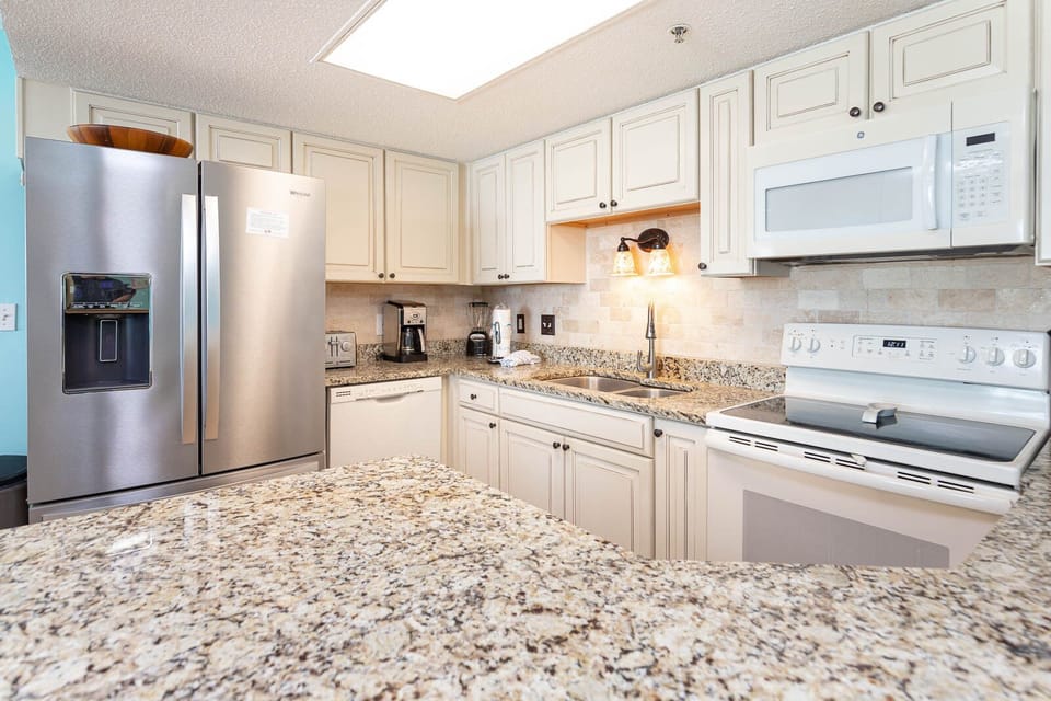 Brightly lit kitchen featuring granite countertops, a sleek refrigerator, and a cozy breakfast bar with seating