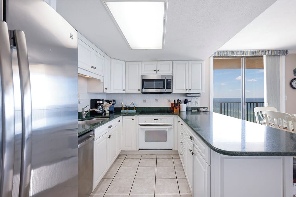 Bright white cabinetry complements the green countertops in this kitchen with a breakfast bar and beach view